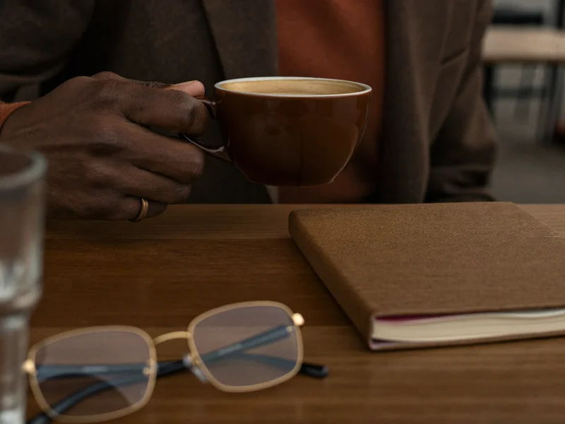 Illustrazione: mani anziane con tazza di caffè e taccuino vuoto
